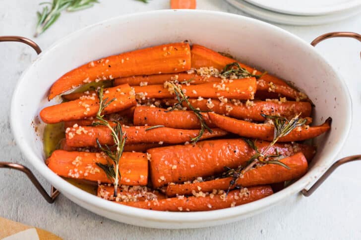 White oval dish filled with roasted carrots with honey, garnished with rosemary.