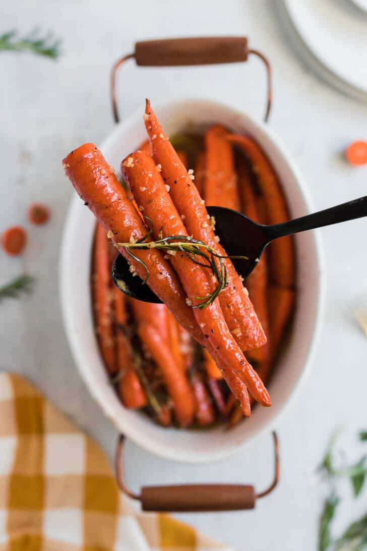 A black spoon lifting roasted root vegetables out of a baking dish.