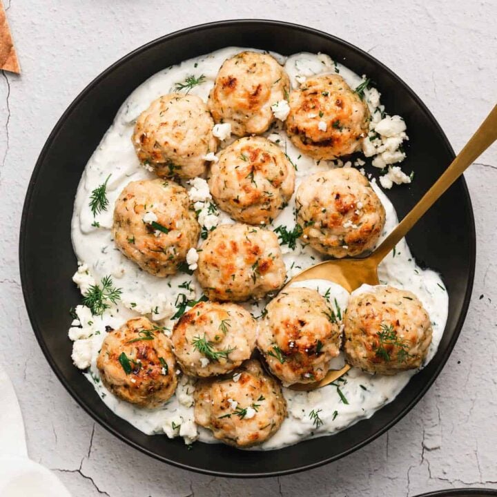 Greek chicken meatballs in a black bowl with yogurt sauce on the bottom.