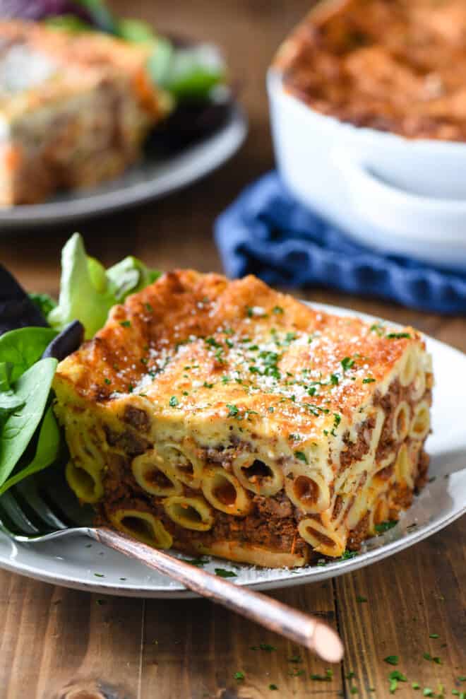 Large slice of Greek lasagna on white plate with green salad.