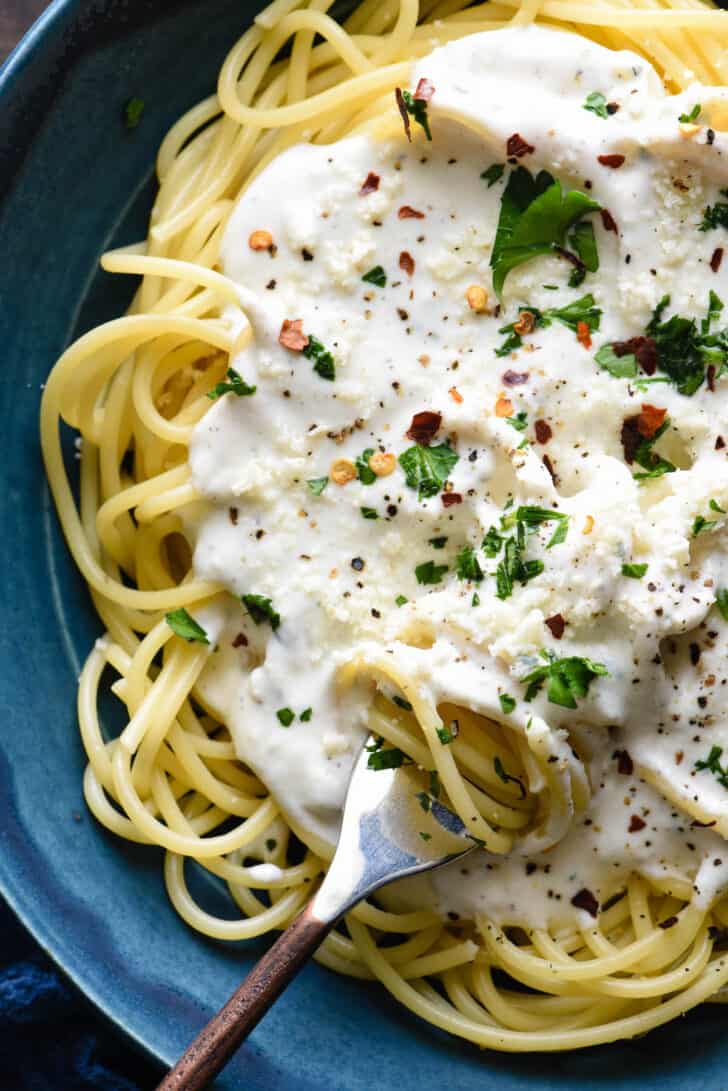 A blue bowl filled with spaghetti topped with Greek yogurt pasta sauce, chopped parsley and red pepper flakes.