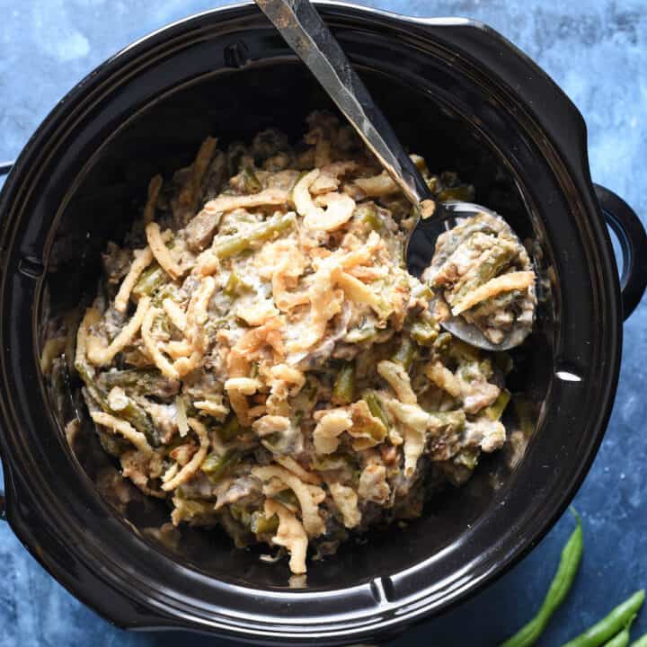 A green bean casserole in crock pot on a blue background.