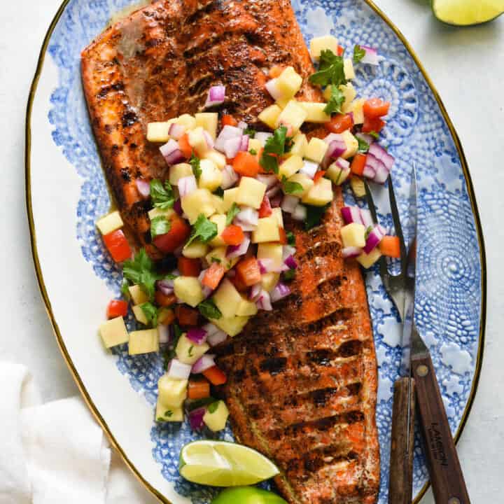 Decorative blue and white platter topped with a large piece of grilled salmon with skin and chopped pineapple salsa.