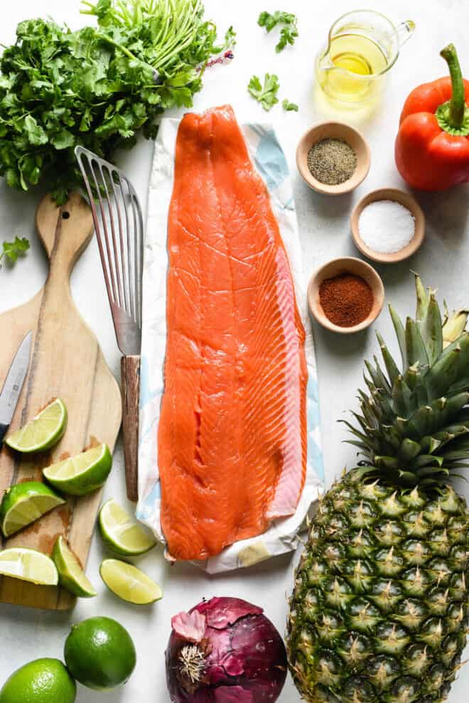 Flat lay of ingredients needed to make grilled sockeye salmon and pineapple salsa, including fruit, herbs and spices.