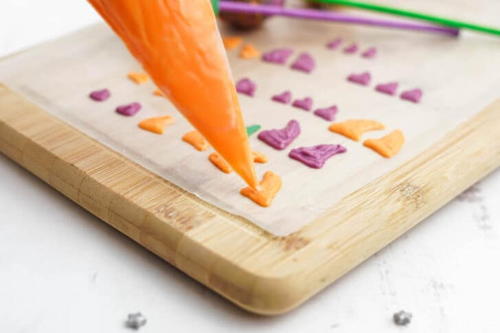 Orange decorations for Halloween cake pops being piped onto wax paper on top of a cutting board.