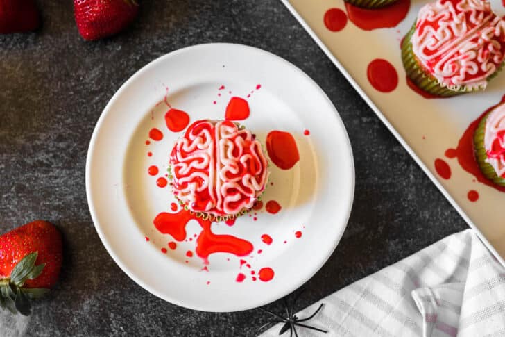 A Halloween cupcake piped with frosting to look like a bloody zombie brain, on a white plate.