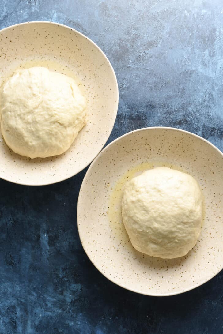 Two large shallow speckled bowls, each with a ball of dough in them.