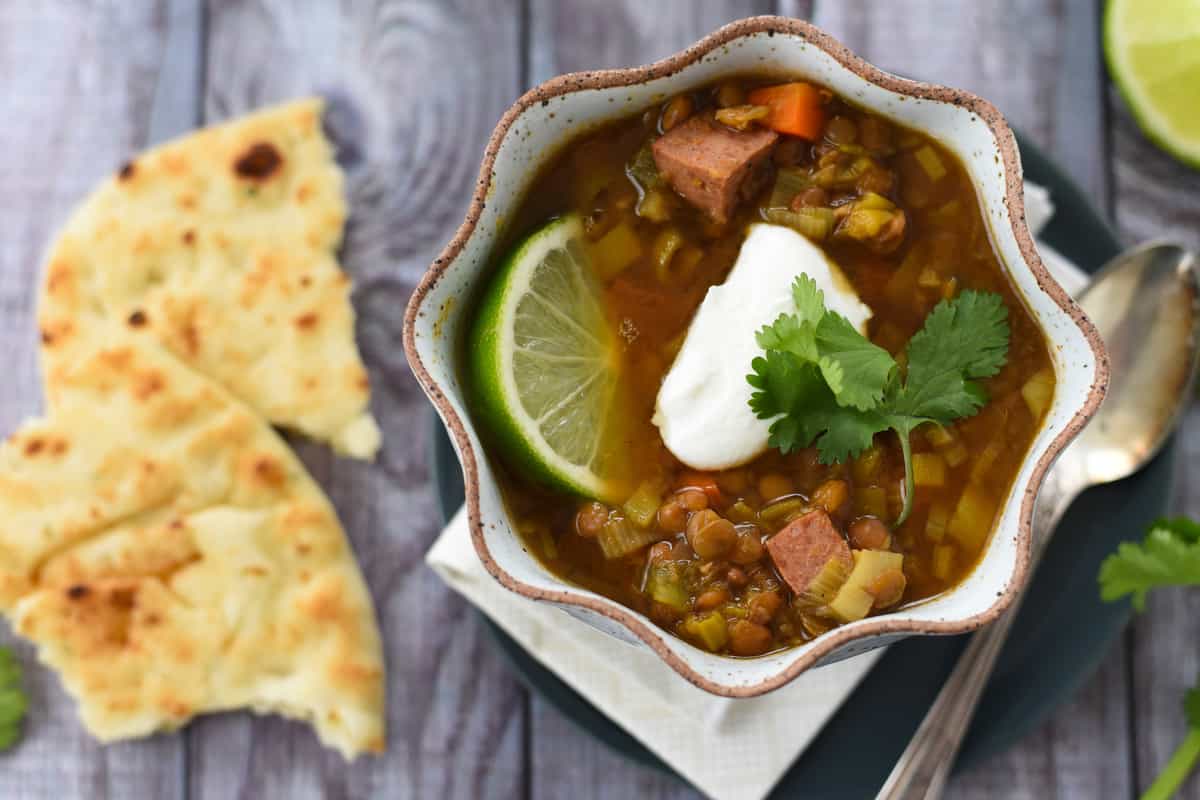 Overhead photo of lentil soup topped with yogurt and cilantro, with naan bread next to it.