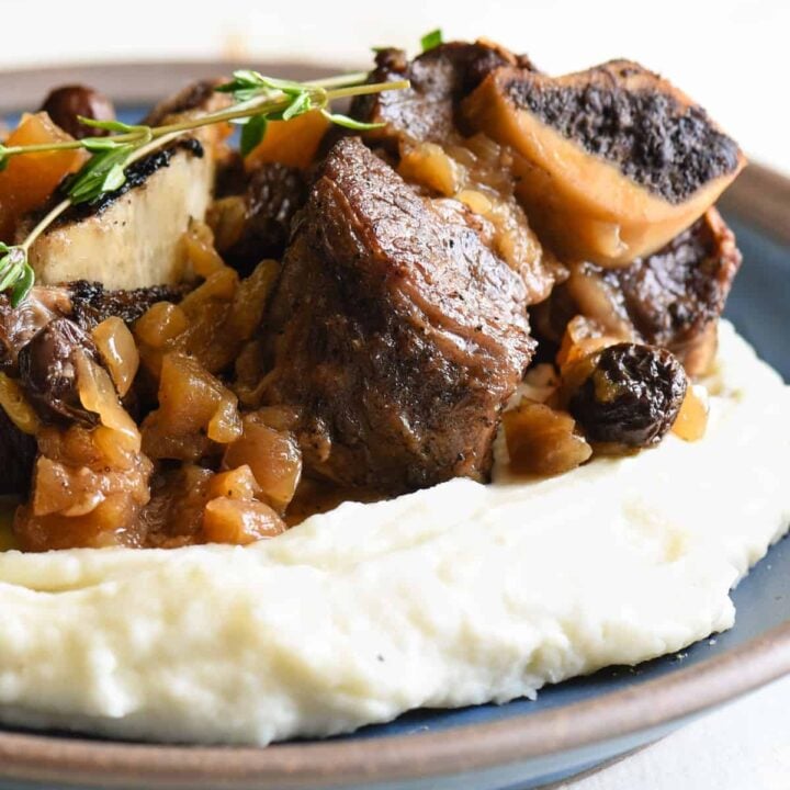 Shallow blue bowl filled with mashed potatoes, topped with Instant Pot short ribs and garnished with thyme.