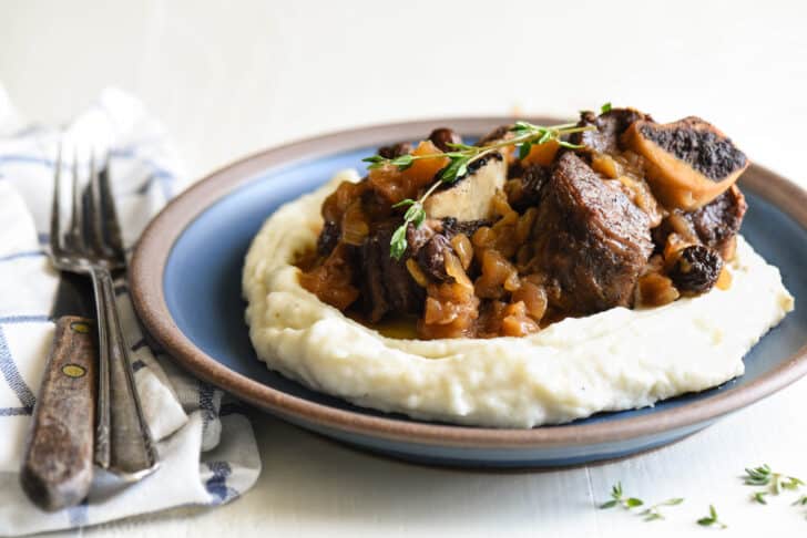 Shallow blue bowl filled with mashed potatoes, topped with Instant Pot braised short ribs and garnished with thyme.