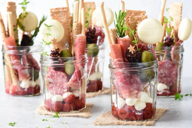 Five servings of jarcuterie, which are glass jars filled with charcuterie, cheese, crackers and condiments.