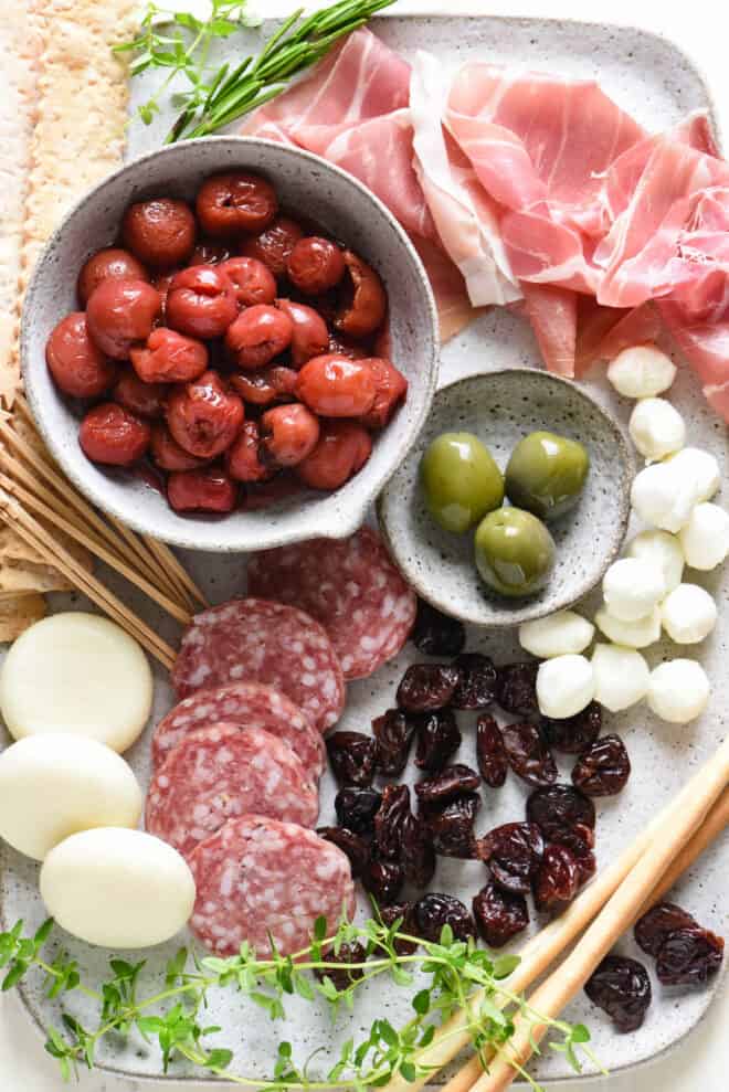 Handmade ceramic platter filled the ingredients for jarcuterie, like charcuterie, cheeses, olives, dried fruit and crackers.