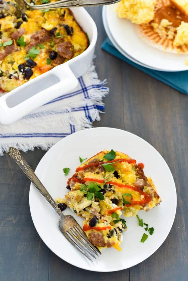 A piece of casserole made with corn bread and eggs on a small white plate with fork.