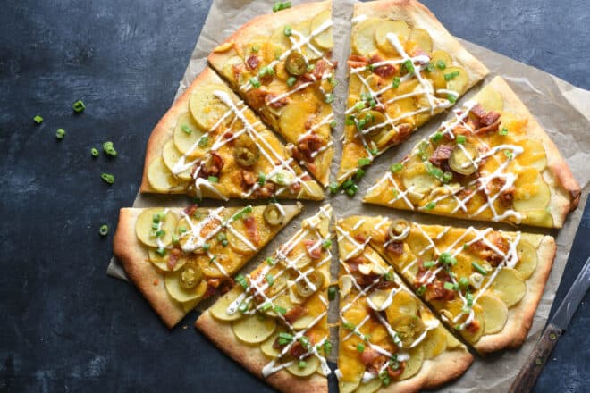 Baked potato pizza cut into eight slices, on dark background.