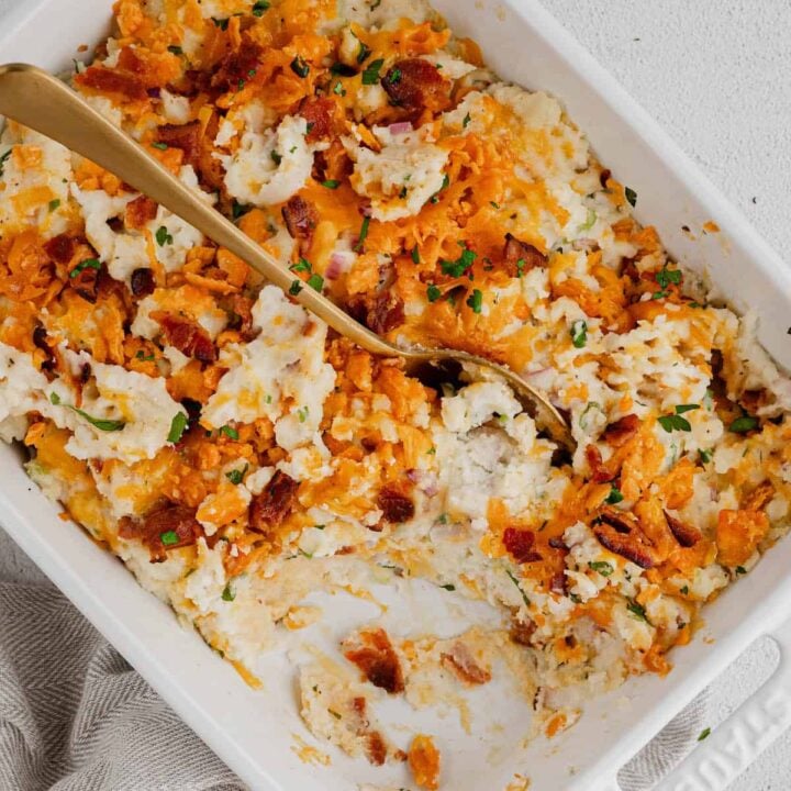 A gold spoon digging into loaded mashed potato casserole in a white baking dish.