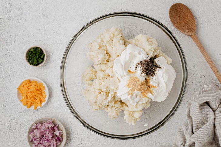 A glass mixing bowl filled with whipped spuds, sour cream, garlic powder and black pepper.