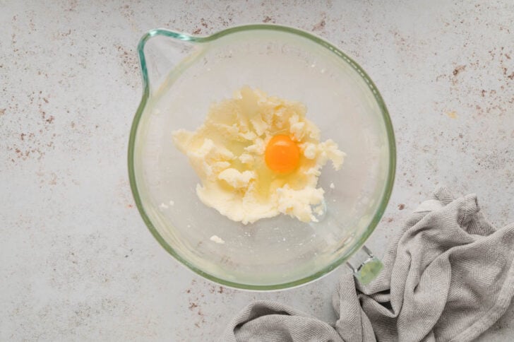 The beginnings of a cookie dough with an egg in the glass bowl of a stand mixer.