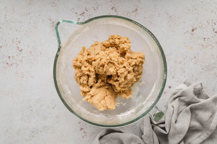 A light brown cookie dough in the glass bowl of a stand mixer.