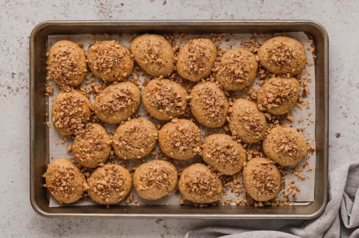 A rimmed baking pan lined with parchment paper, topped with melomakarona.