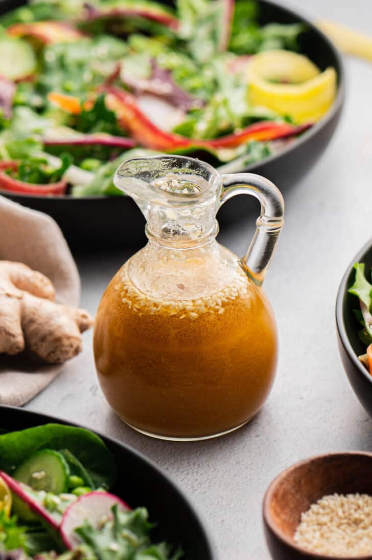 Miso ginger dressing in a small glass carafe, with a fresh vegetable salad in the background.