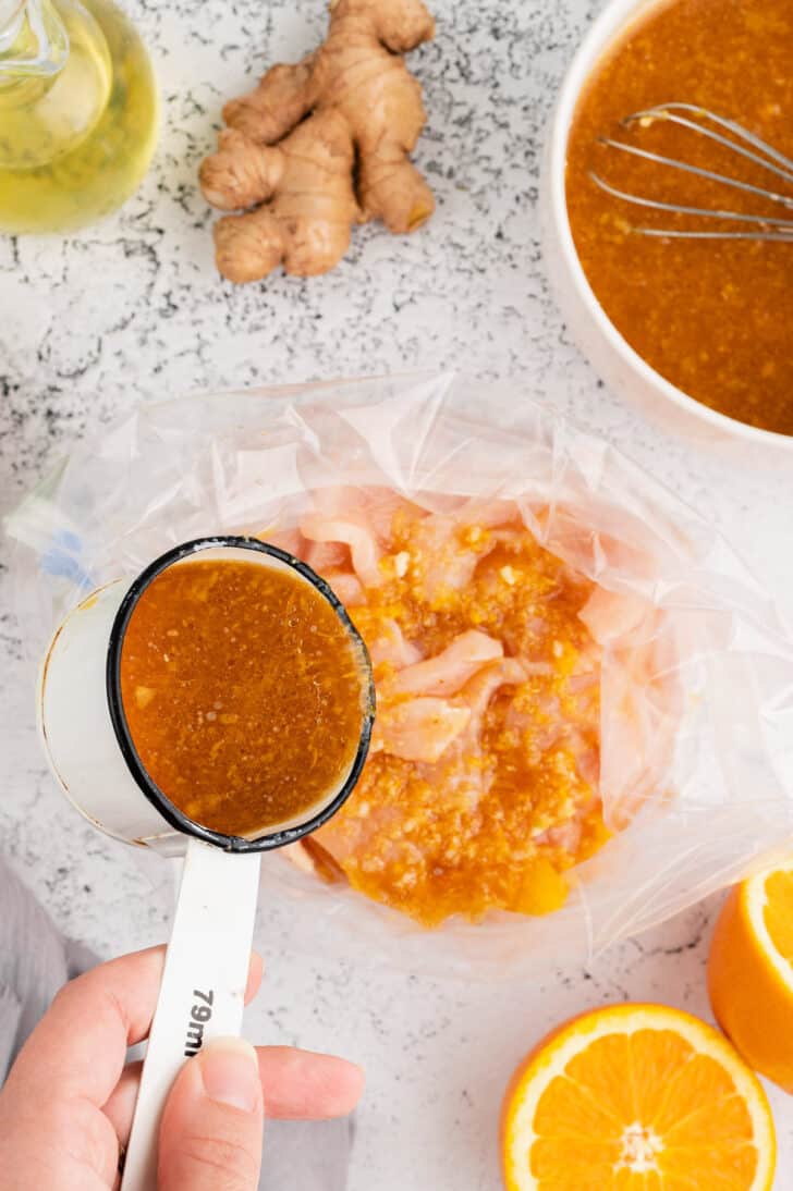 Orange juice marinade being poured over sliced raw chicken in a plastic zip top bag.