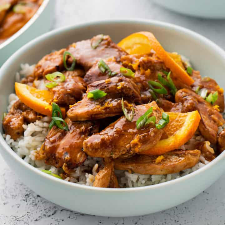 White rice topped with chicken and orange ginger sauce in a white bowl.