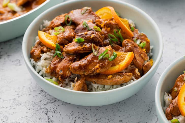 White rice topped with chicken and orange ginger sauce in a white bowl.