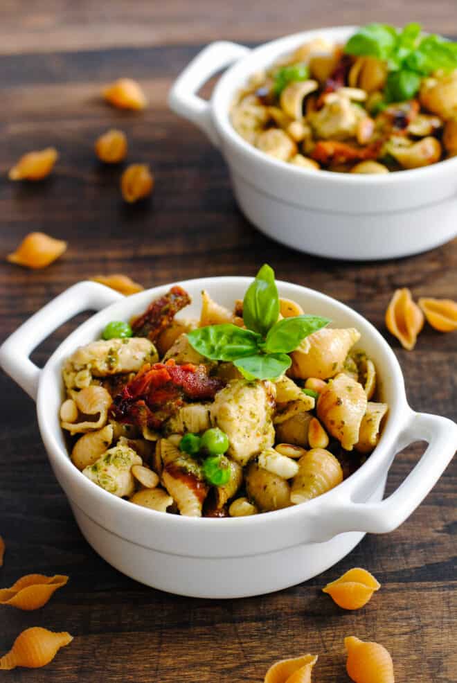 Small white ceramic dishes with handles, filled with pesto pasta with veggies and chicken.