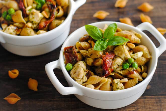 Small white ceramic dishes with handles, filled with pesto pasta with veggies and chicken.