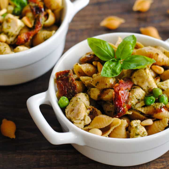 Small white ceramic dishes with handles, filled with pesto pasta with veggies and chicken.