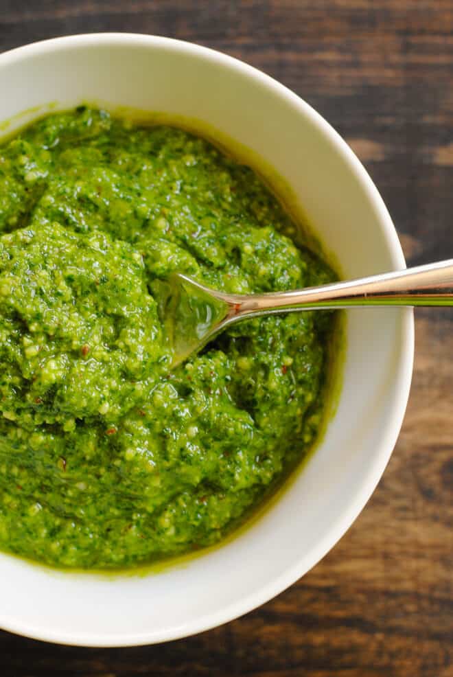 White bowl filled with green pesto with spoon in it.