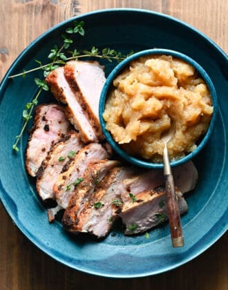 Shallow blue bowl filled with sliced pork chops and applesauce.