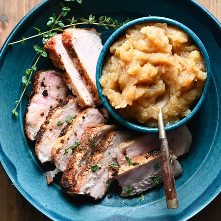 Shallow blue bowl filled with sliced pork chops and applesauce.