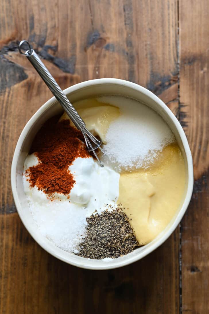 A bowl with dressing ingredients layered into it, including mayonnaise, sour cream, sugar and spices.