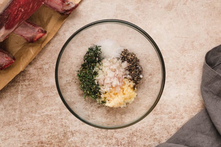 A glass bowl filled with herbs, spices, garlic and shallots.