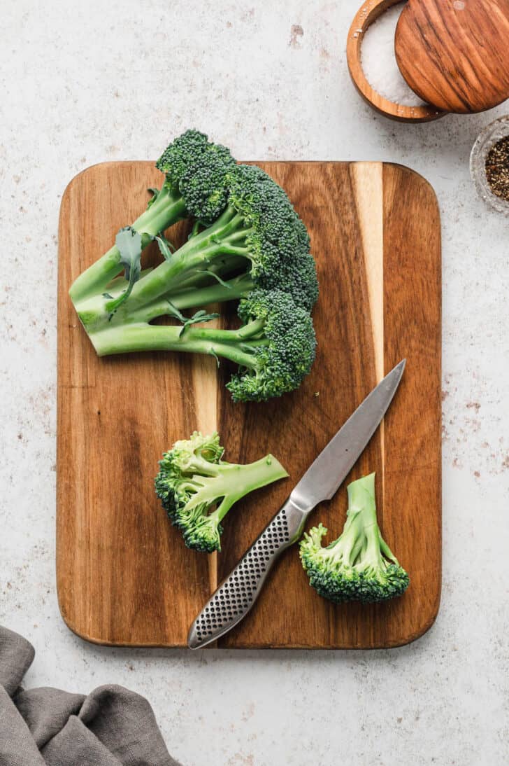 A head of green brassica vegetable on a wooden cutting board being cut into small florets.