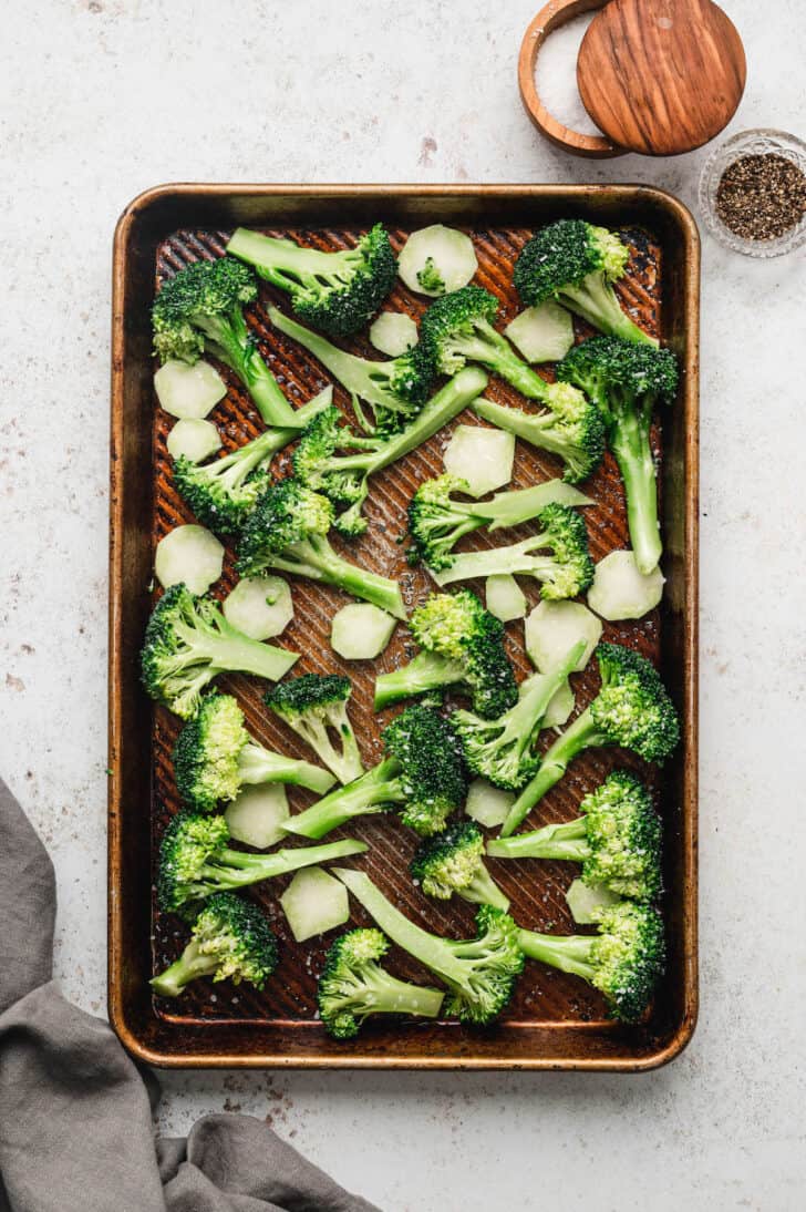 Roasted broccoli florets and cross sections of stems on a rimmed textured baking pan.