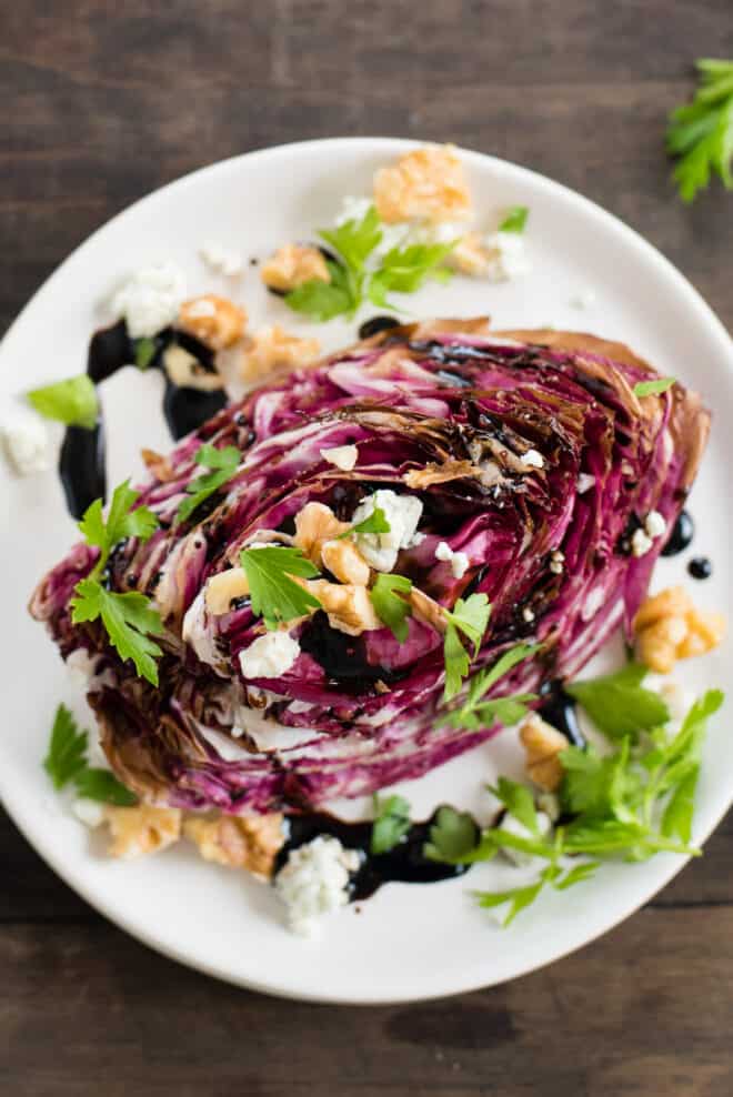 White plate topped with wedge of roasted purple radicchio, topped with cheese, nuts and herbs.