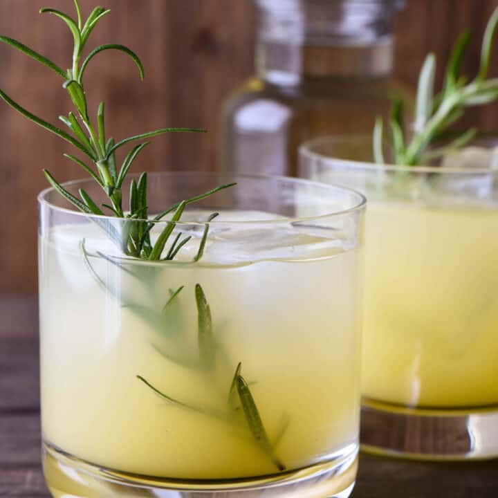 Orange hued cocktail in small glass with a rosemary sprig garnish.