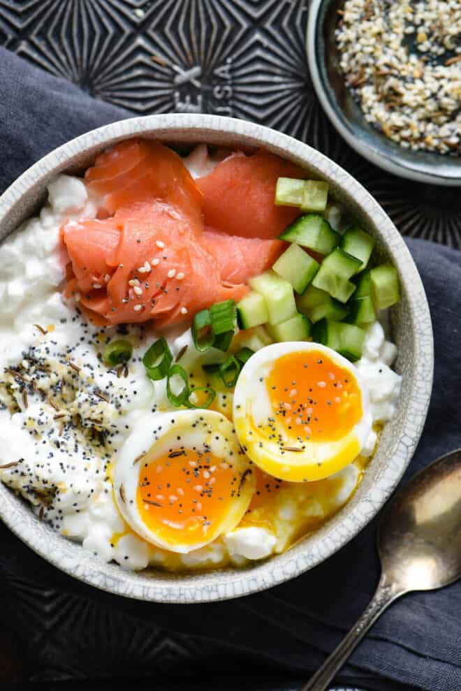 Gray bowl filled with cottage cheese, soft egg, smoked salmon and green onions.