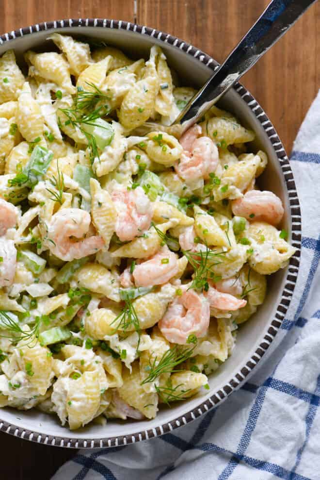 Serving bowl filled with seafood pasta salad, with serving spoon in it.