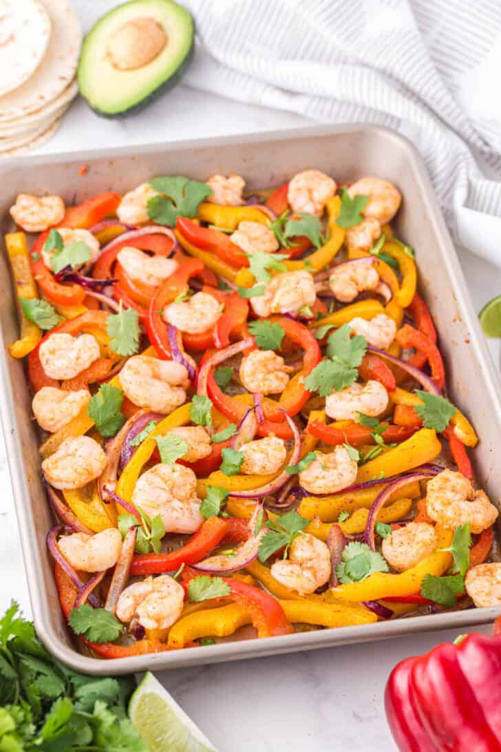 Sheet pan shrimp fajita recipe sprinkled with cilantro on a light marble surface.