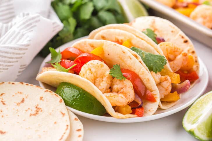 Three flour tortillas filled with shrimp fajitas and cilantro, on a white plate.