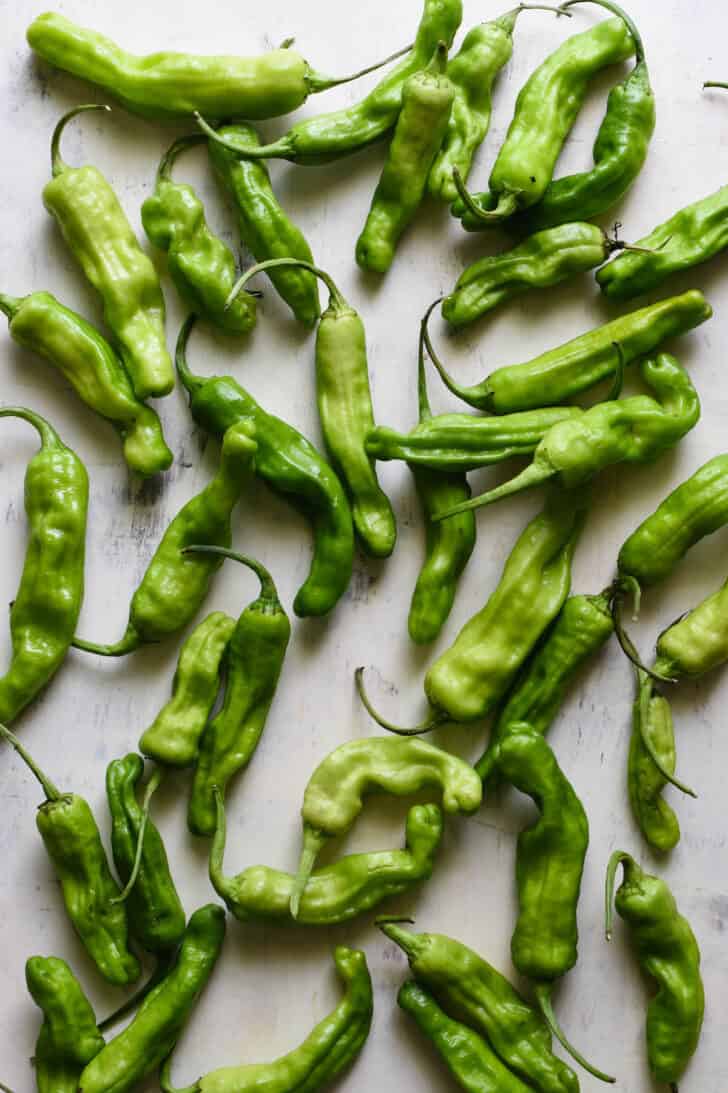 Raw shishito peppers on a light surface.