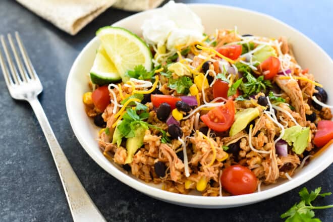 Shallow white bowl filled with rice, beans, chicken and other burrito fixings.