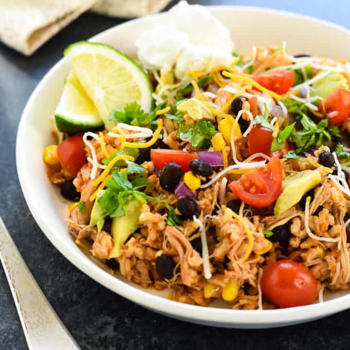 Shallow white bowl filled with rice, beans, chicken and other burrito fixings.