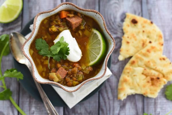 Overhead photo of lentil soup on grey picnic table surface, with naan bread on side.