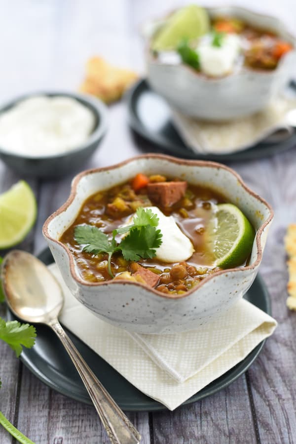 Slow cooker lentil soup with sausage in fluted bowl, topped with cilantro, yogurt and a lime wedge.