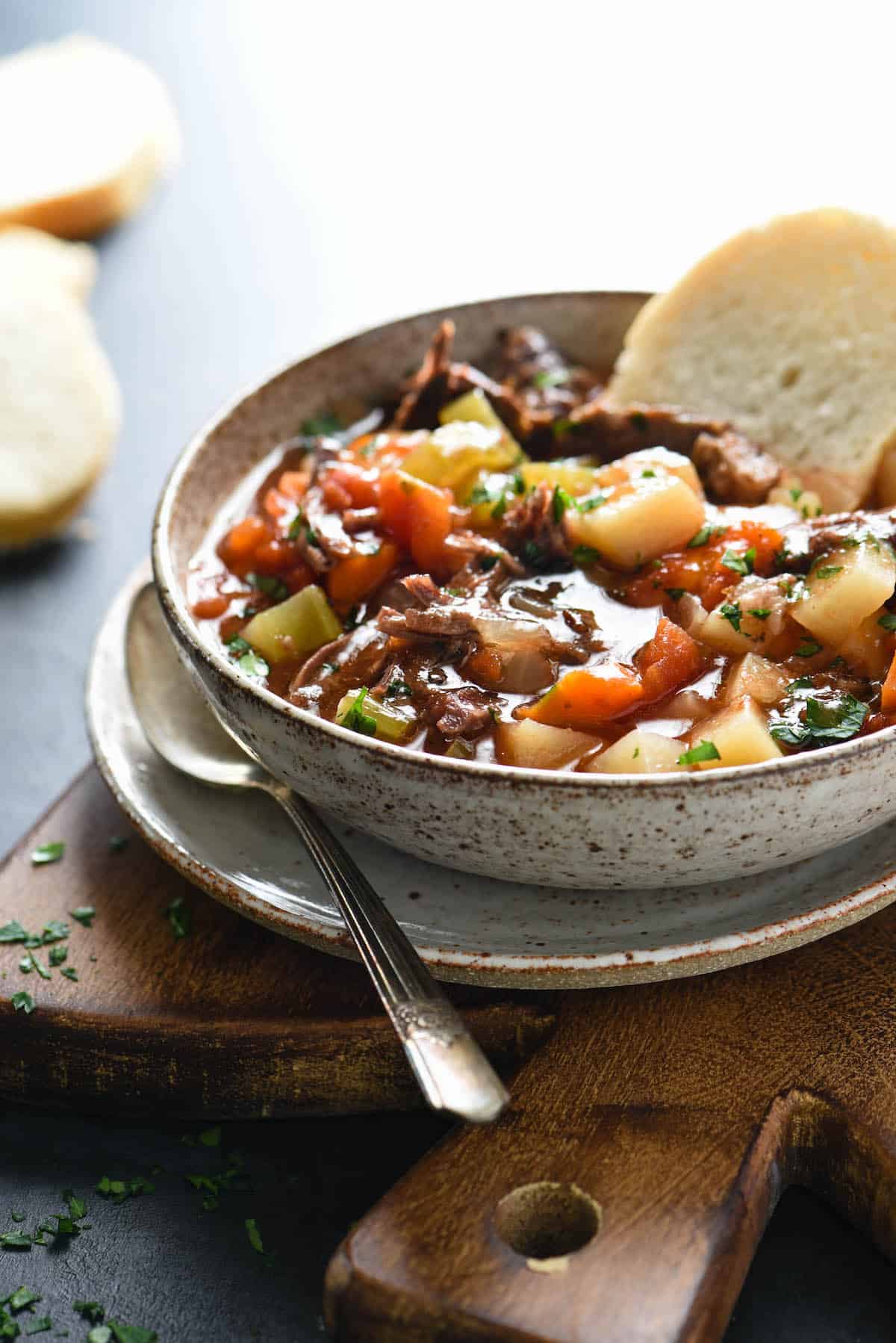 Bowl of beef and vegetable soup with bread dunked into it.