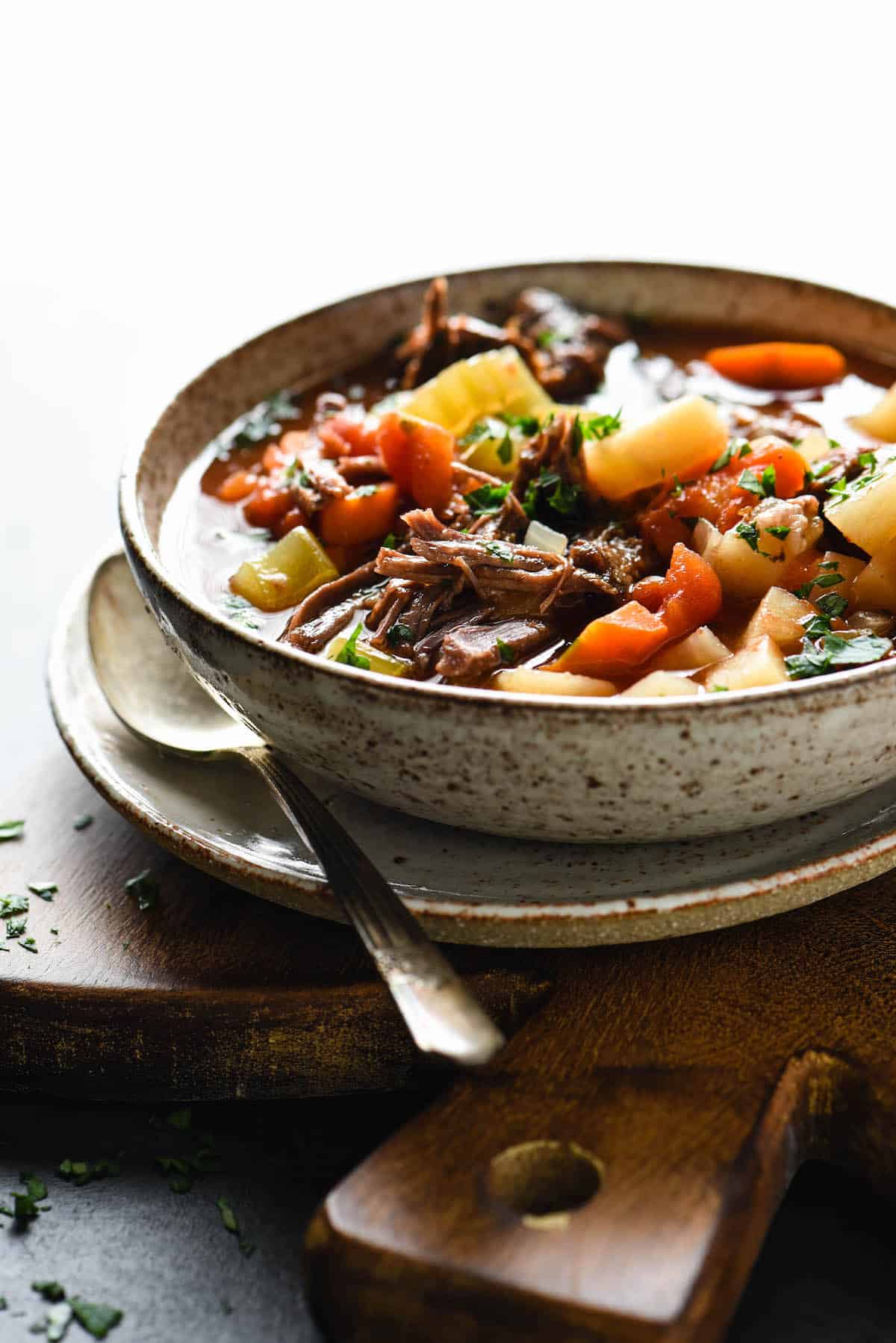 Bowl of Crockpot Vegetable Beef Soup on plate on top of cutting board.